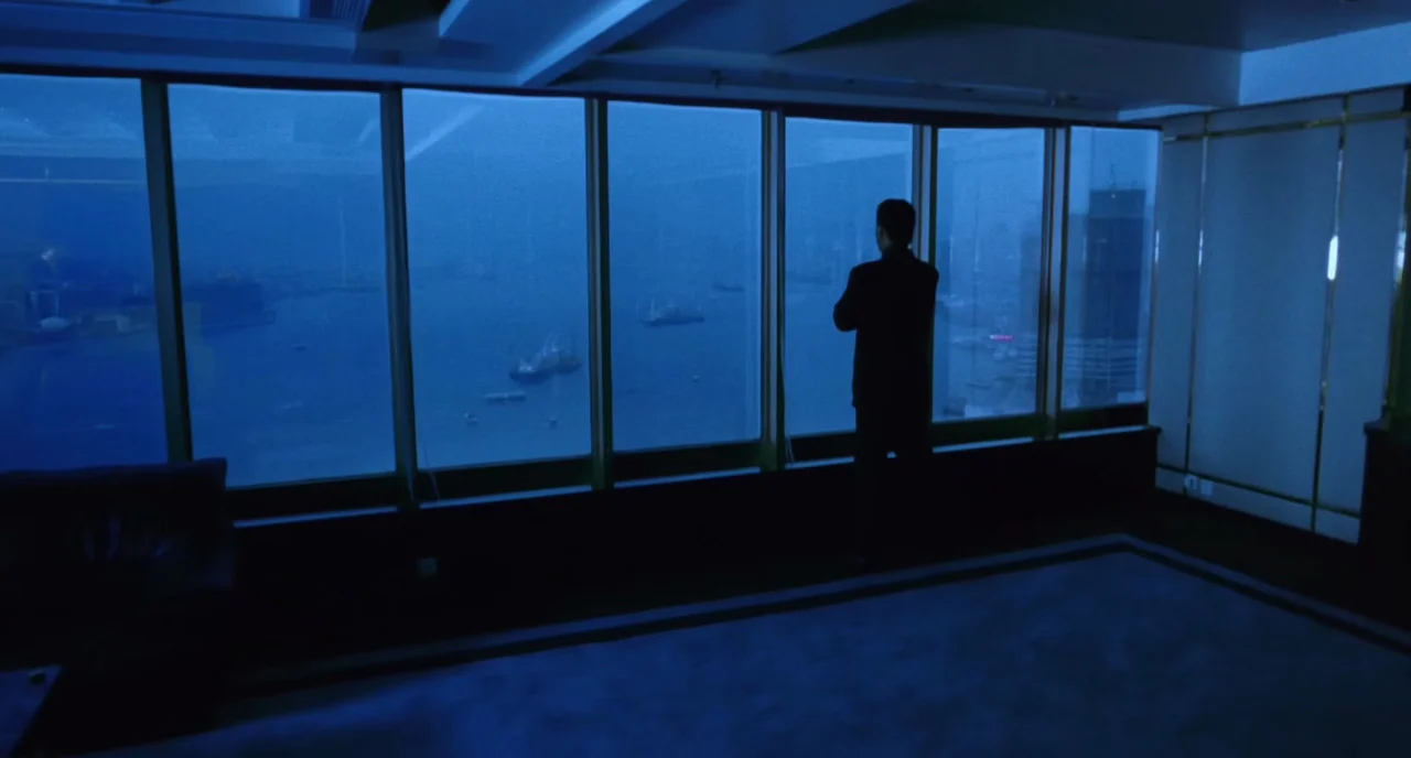 The Killer (1989) movie still: wide — A dark, modern luxury apartment interior features floor-to-ceiling windows looking out over a harbor. A man in…
