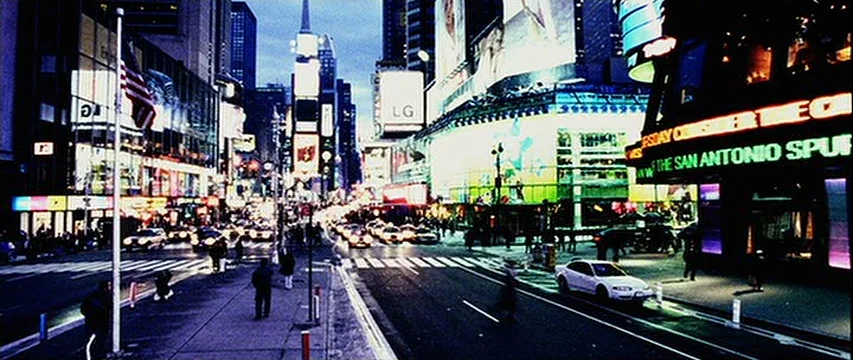 25th Hour (2002) movie still: wide — A dense urban thoroughfare at night is crowded with glowing commercial advertisements and billboards. Cars and…