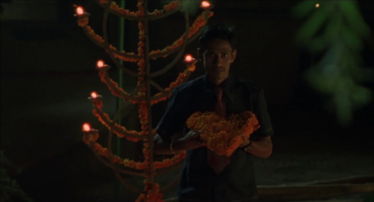 Monsoon Wedding (2001) movie still: medium — A man stands in darkness at night near a decorative lit lamp stand. He holds a large heart-shaped…