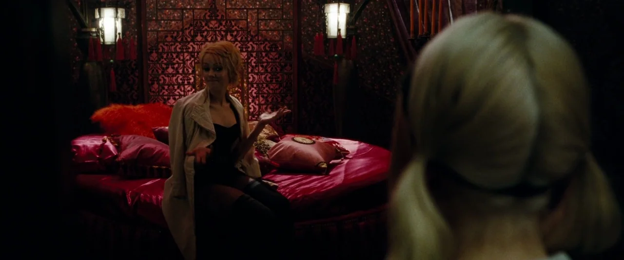 Sucker Punch (2011) movie still: medium — A dark boudoir features a large round red bed and patterned oriental screens. A young blonde woman sits on…