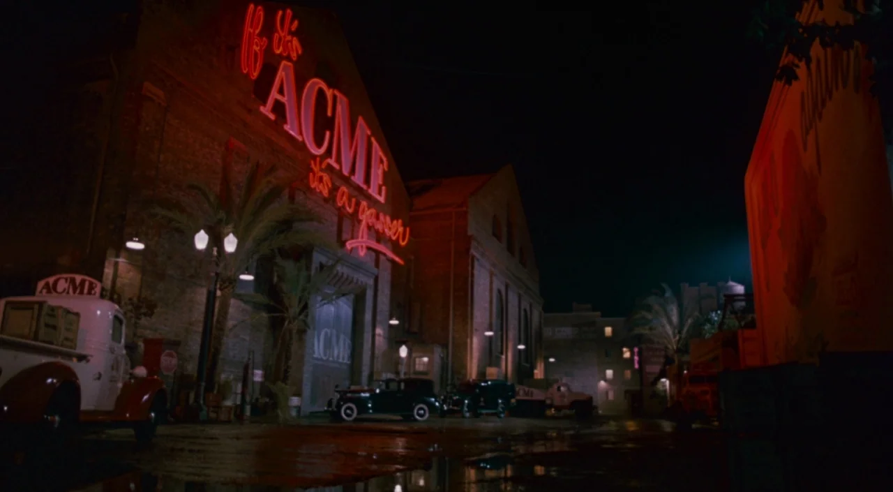 Who Framed Roger Rabbit (1988) movie still: establishing — A night view of a brick factory building features a large, glowing red ACME neon sign. A…