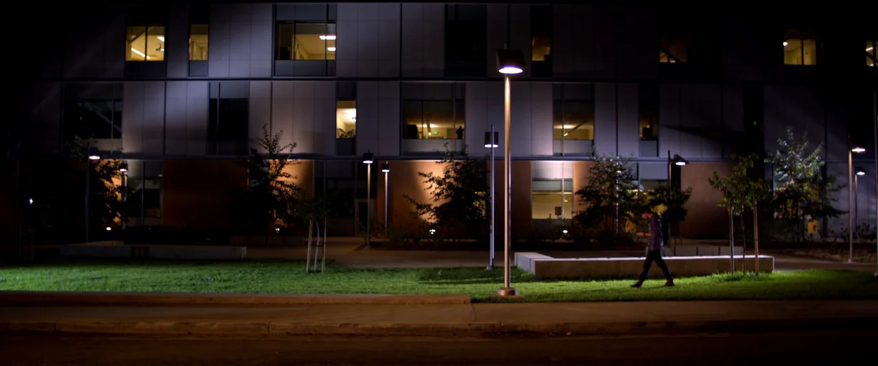 Kaboom (2010) movie still: wide — A modern building with large glass windows overlooks a manicured lawn at night. A lone person walks across the…