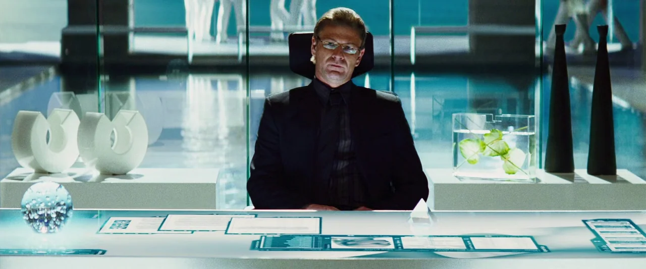 The Island (2005) movie still: medium — A minimalist, glass-walled office features a bright, illuminated touchscreen desk holding various documents…