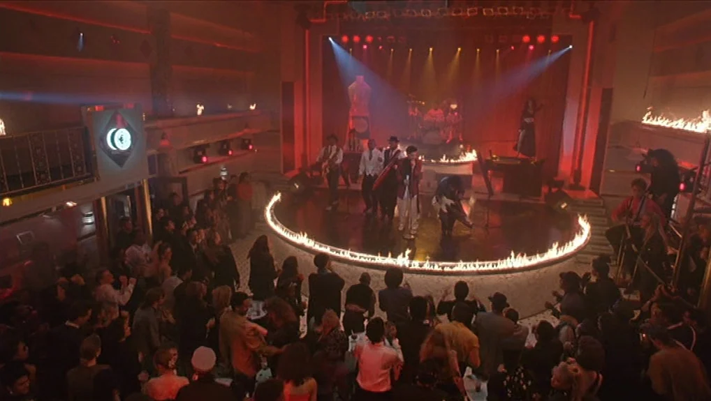 Graffiti Bridge (1990) movie still: wide — A crowded nightclub features a circular stage bordered by a ring of active flames. A musical group…