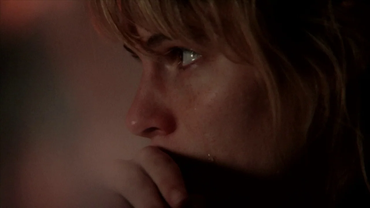 A Horrible Way To Die (2010) movie still: closeup — A dark, dimly lit indoor space with low-key lighting. A woman with blonde hair looks to the side…