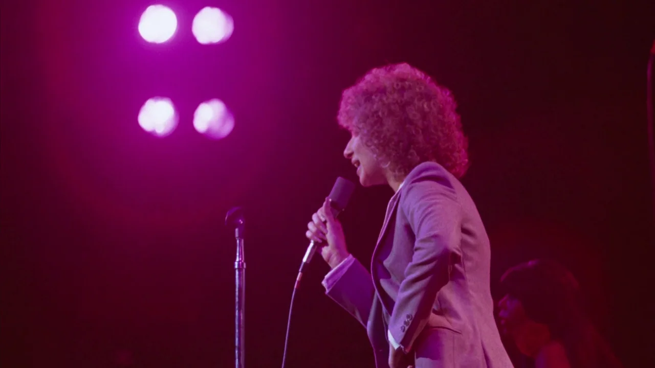 A Star Is Born (1976) movie still: medium — A dimly lit musical performance space featuring high-intensity magenta spotlights. A female performer…