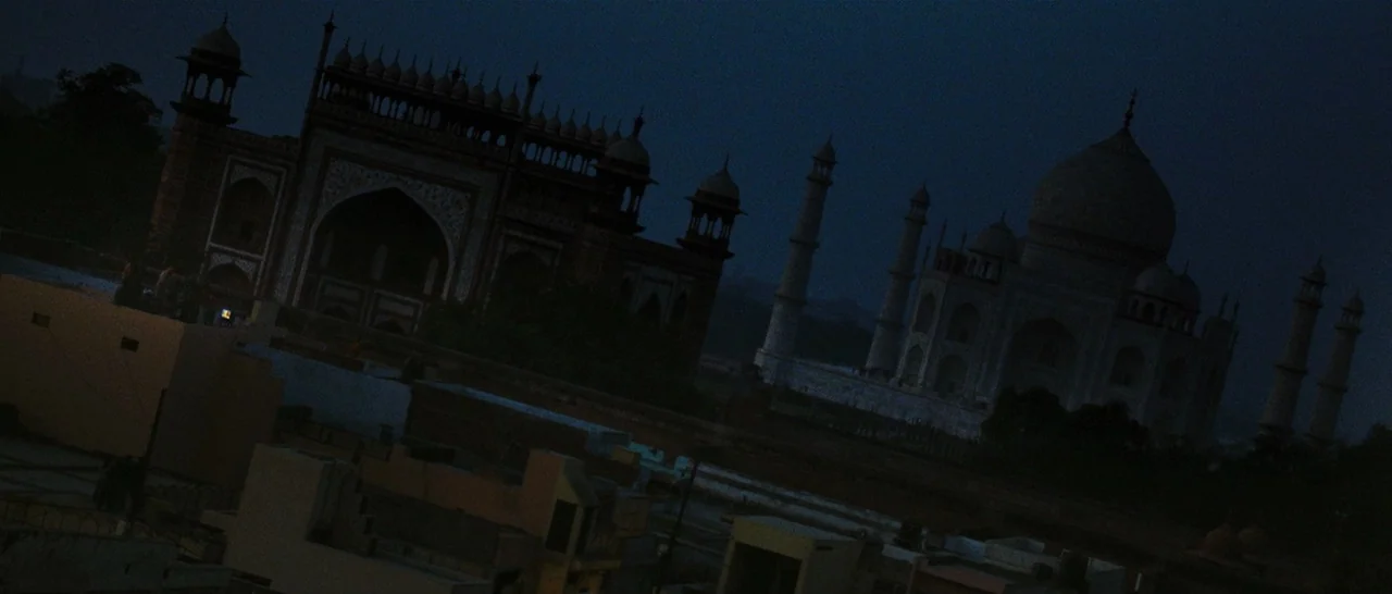 Slumdog Millionaire (2008) movie still: establishing — The Taj Mahal and its surrounding mosque complex stand illuminated in the dark night.…