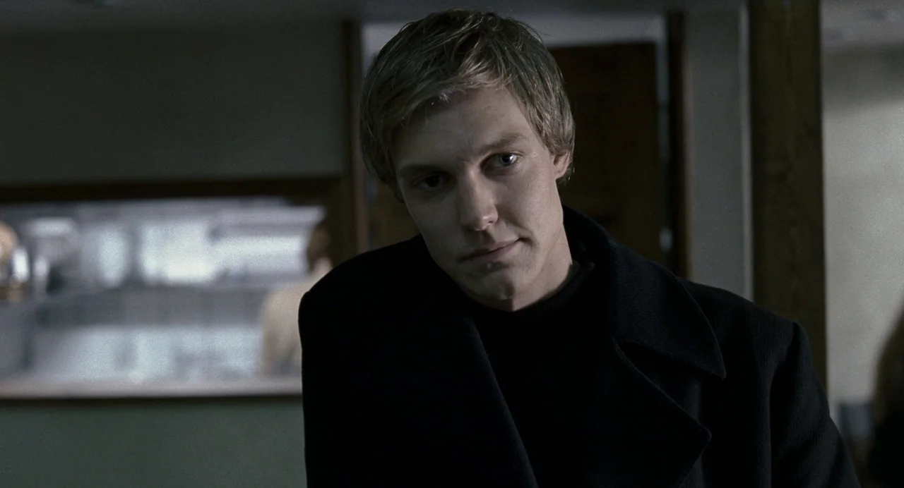 Reprise (2006) movie still: closeup — A dimly lit indoor space with blurred background architectural lines and soft shadows. A man with short blonde…