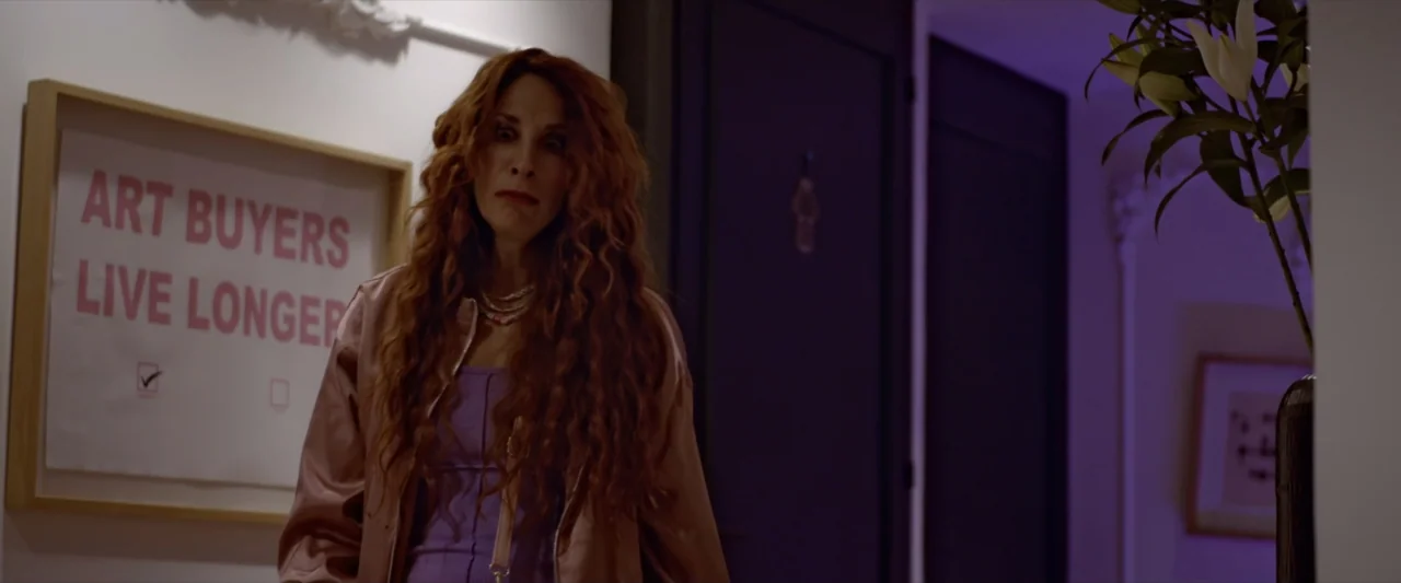 Like or Die (2023) movie still: medium — A dimly lit residential hallway features a framed print on the white wall. A woman with long red hair…