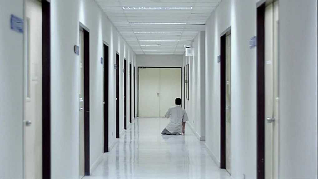 Syndromes and a Century (2006) movie still: wide — A long, symmetrical hospital corridor features white walls and a polished reflective floor. A…