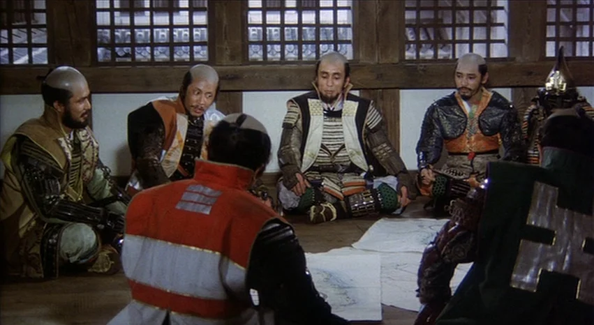 Kagemusha (1980) movie still: wide — A wooden interior room with lattice windows features six men in samurai armor. They sit in a circle on the…