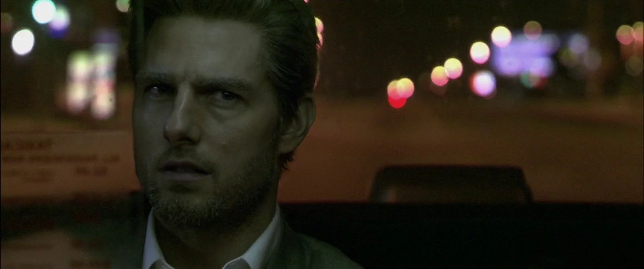 Collateral (2004) movie still: closeup — A man sits in the back of a vehicle at night. Bokeh light streaks are visible through the window.