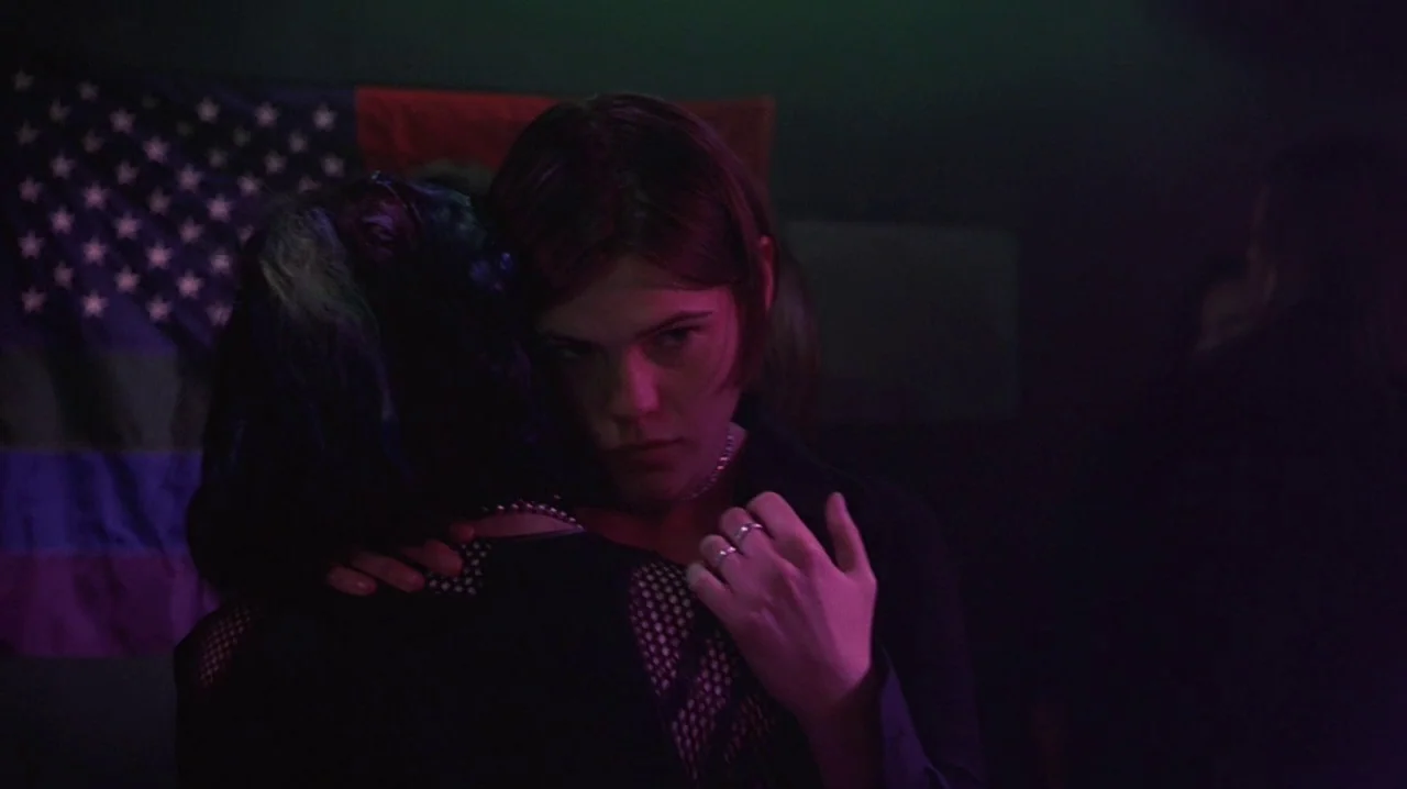 But I’m A Cheerleader (1999) movie still: medium — A dimly lit, hazy interior space with a partially visible American flag on the wall. Two women…