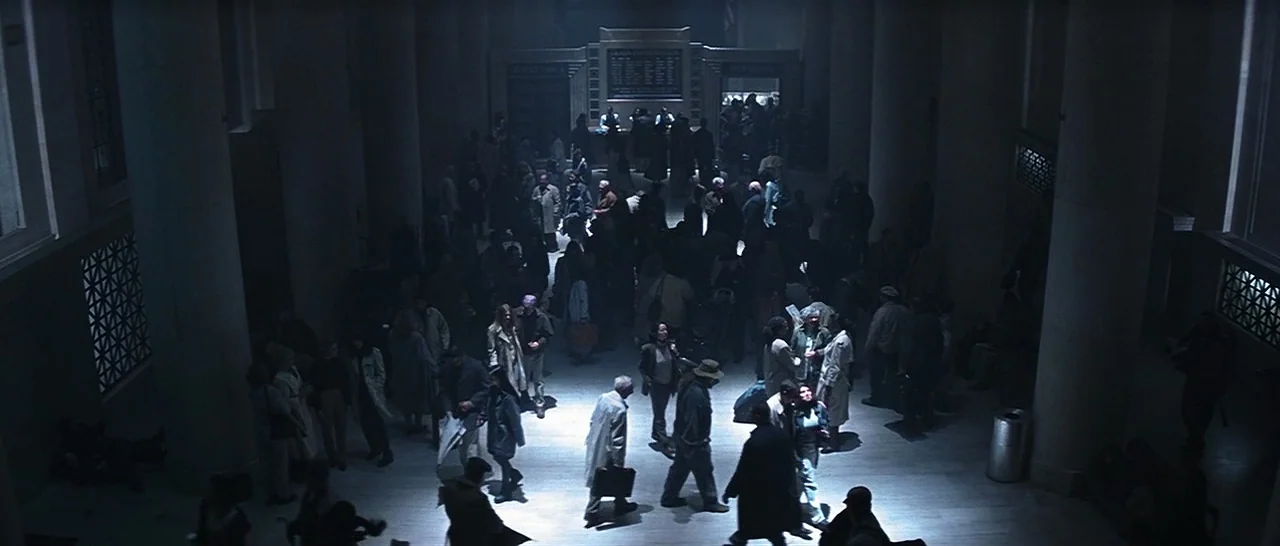 Unbreakable (2000) movie still: wide — A spacious train terminal concourse features large stone columns and an overhead digital information sign. A…