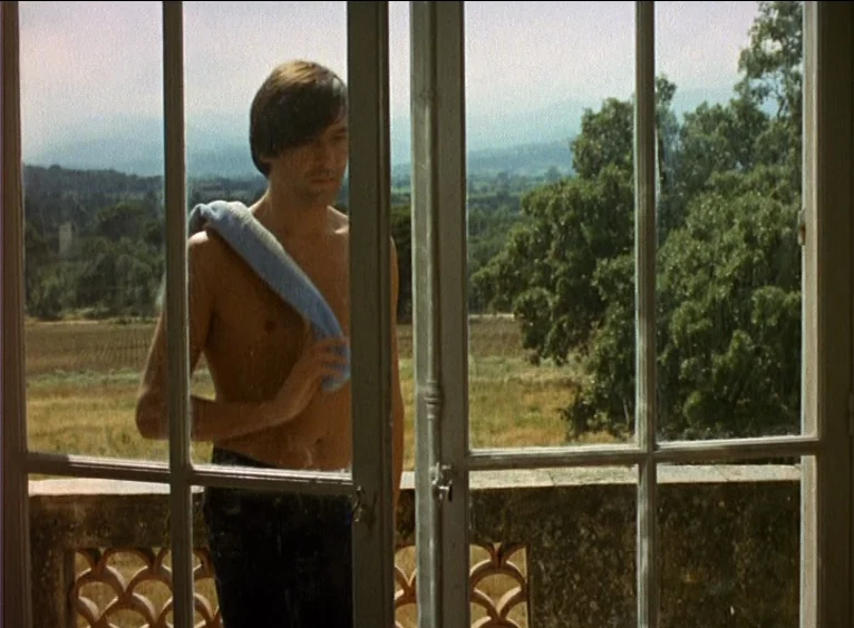 La Collectionneuse (1967) movie still: medium — A stone balcony overlooks a rural valley with trees and fields in the distance. A shirtless man…