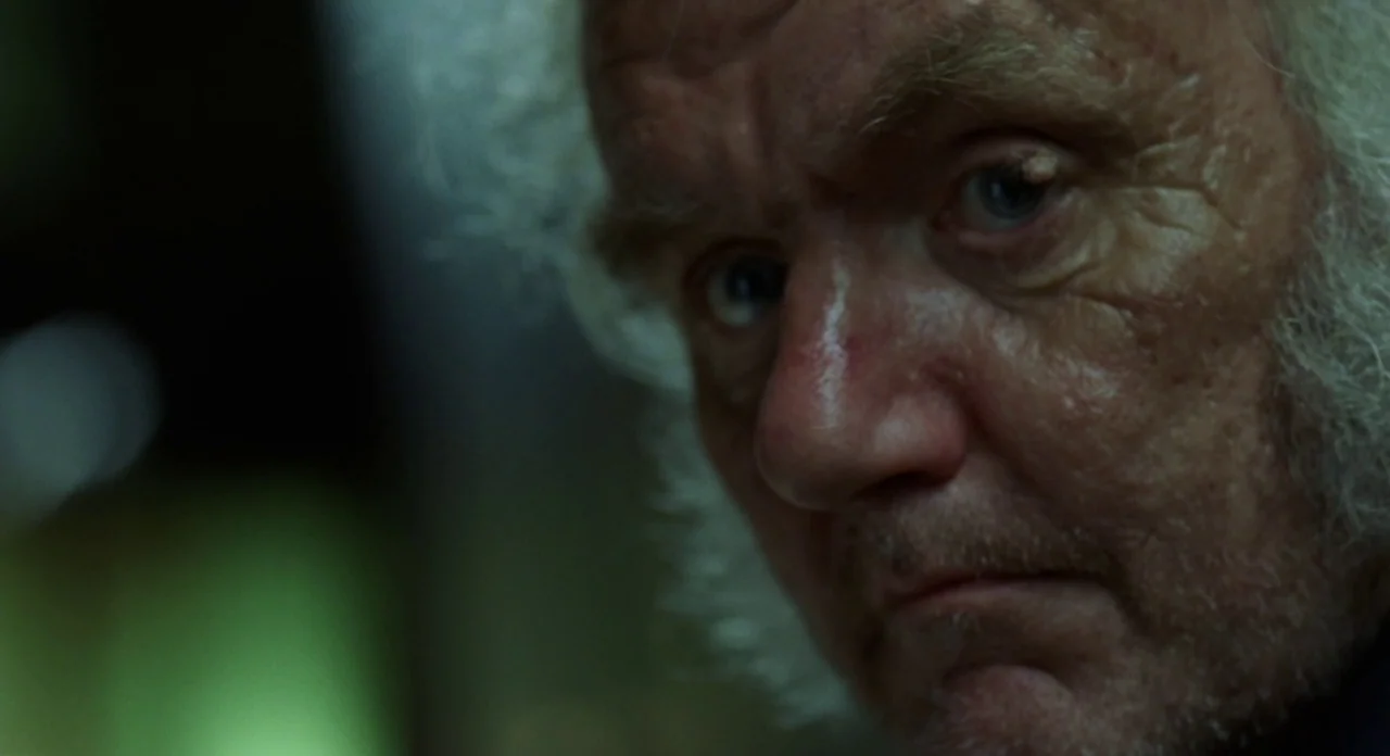 London Boulevard (2010) movie still: closeup — The frame shows an extreme close-up of an elderly man's face in low lighting. He gazes off-camera…
