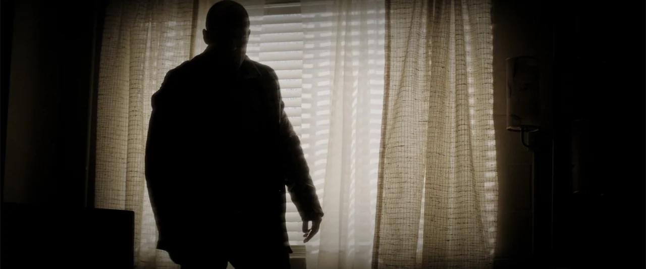 Wild Card (2015) movie still: medium — A dimly lit room features a window dressed with sheer curtains and blinds. A man stands in front of the…