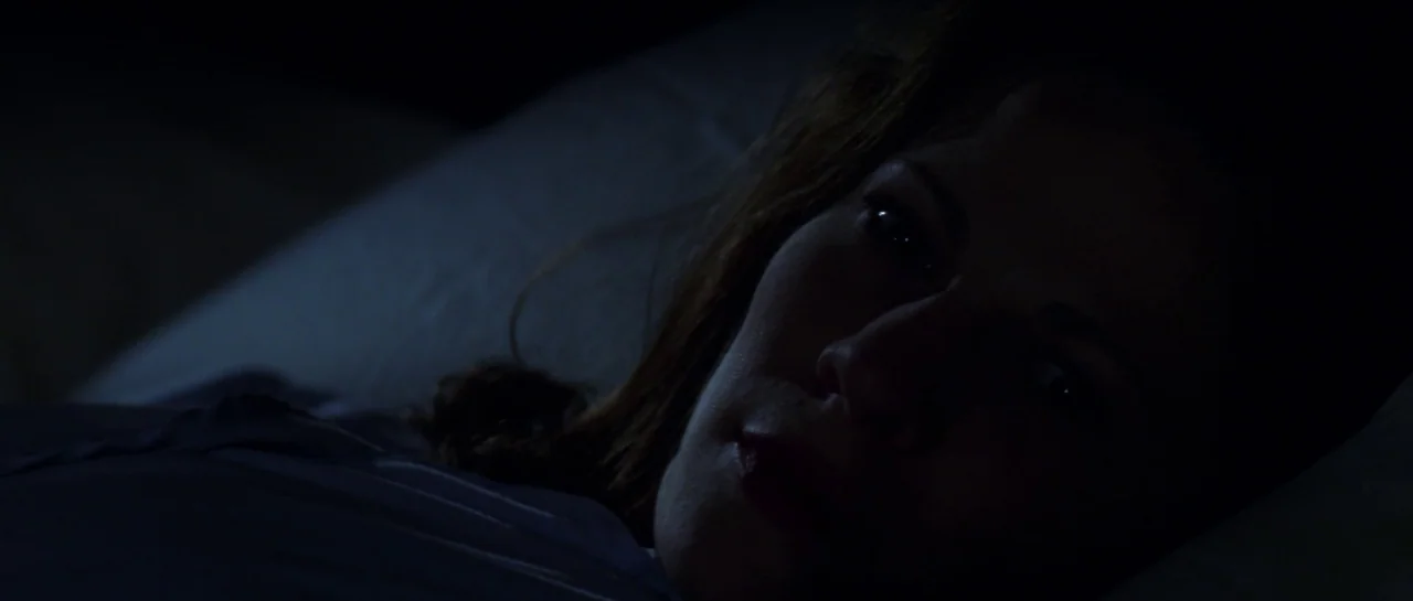 The Haunting (1999) movie still: closeup — A dark, dimly lit bedroom provides a minimal backdrop for a person at rest. A woman lies on a pillow…