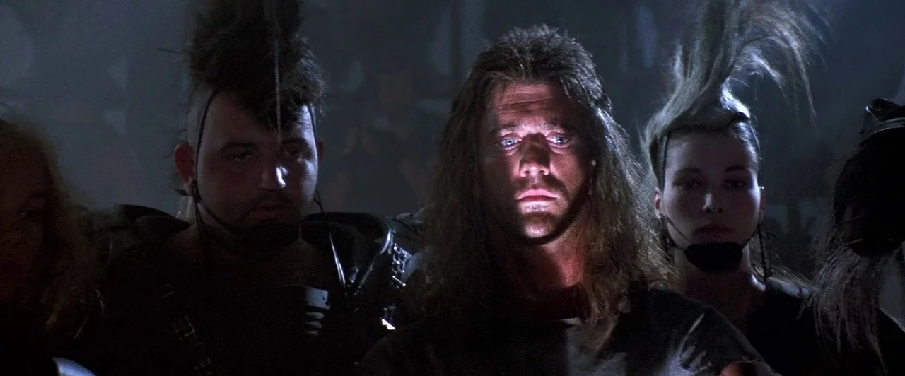 Mad Max Beyond Thunderdome (1985) movie still: medium — A dark, crowded interior space features three people with distinct punk-influenced…