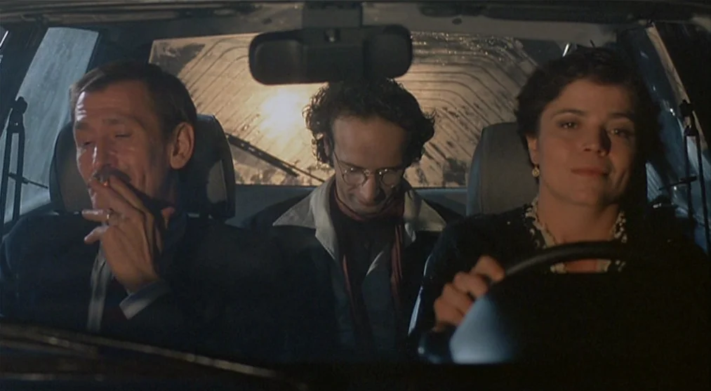The Voice of the Moon (1990) movie still: medium — The interior of a car at night seen from the front windshield. Three people sit inside the…
