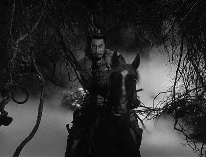 Throne of Blood (1957) movie still: medium — A dense, foggy forest filled with tangled branches and low-hanging tree limbs at night. A samurai…