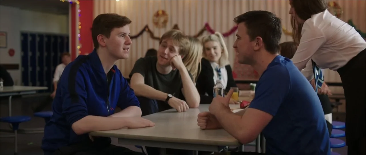 Anna and the Apocalypse (2018) movie still: medium — A school cafeteria features long tables with blue stools and decorative holiday streamers…