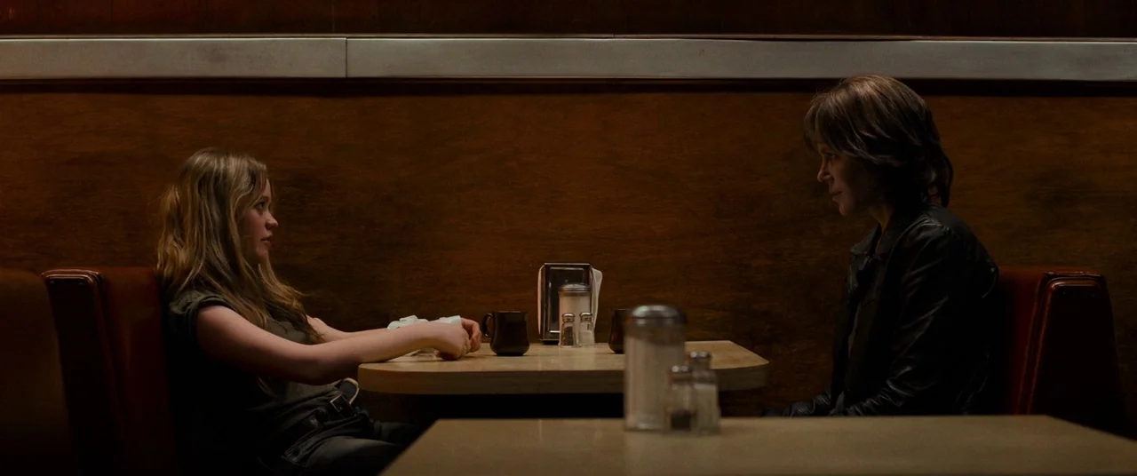 Destroyer (2018) movie still: medium — A dark diner booth features wood-paneled walls and a small rectangular Formica table. Two women sit across…