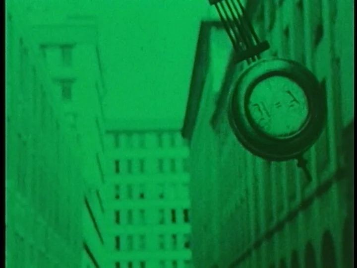 The Cage (1964) movie still: wide — Tall, nondescript buildings frame a narrow urban canyon under dark night conditions. A prominent circular sign…