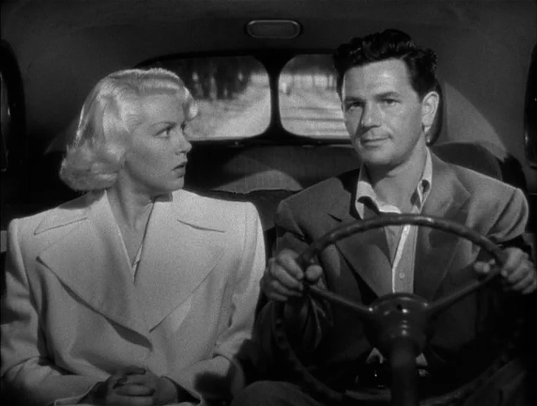 The Postman Always Rings Twice (1946) movie still: medium — A man and woman sit inside the front seats of a 1940s style automobile. The man grips…
