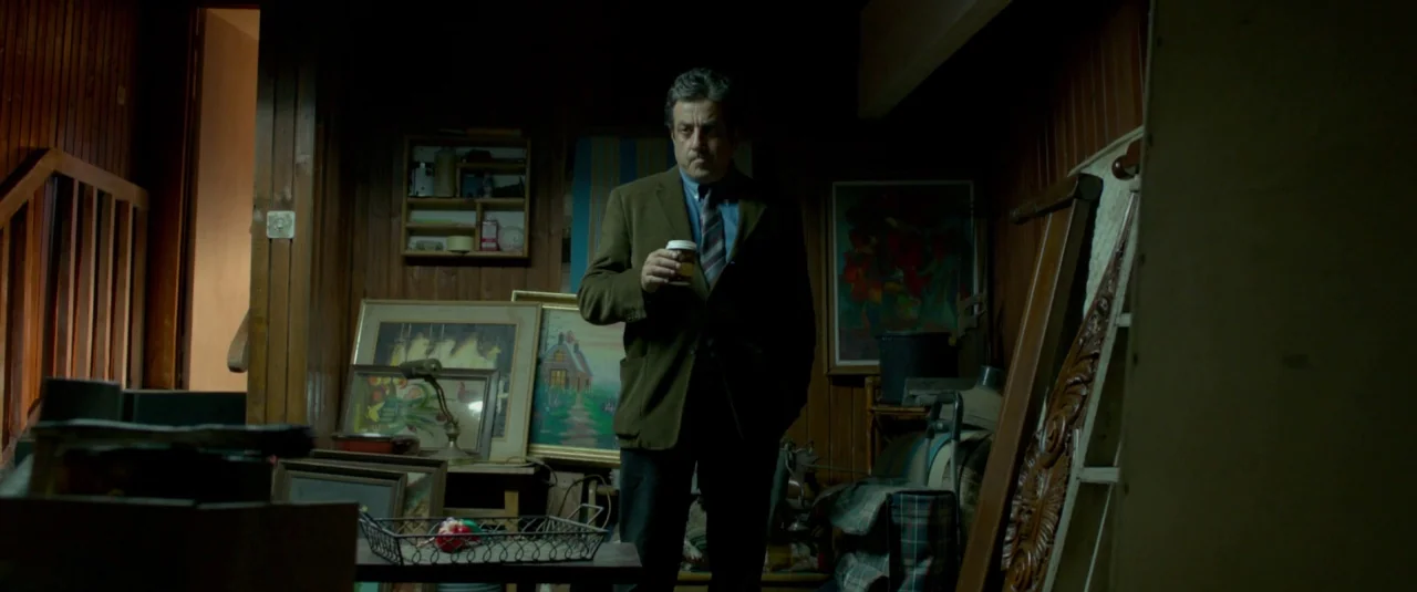 Big Bad Wolves (2013) movie still: medium — A cluttered, dark basement filled with wooden wall paneling, various framed paintings, and furniture. A…