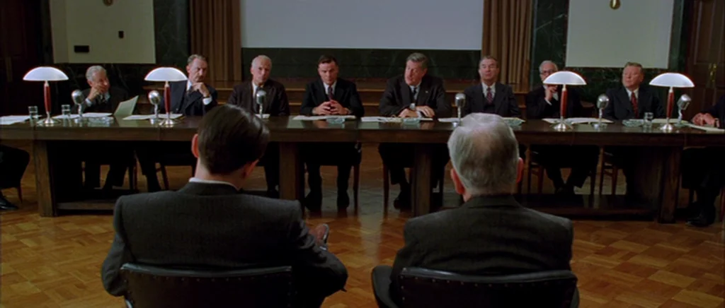 The Aviator (2004) movie still: wide — A formal meeting occurs in a wood-paneled room with a long table. Many men in dark suits sit facing the…