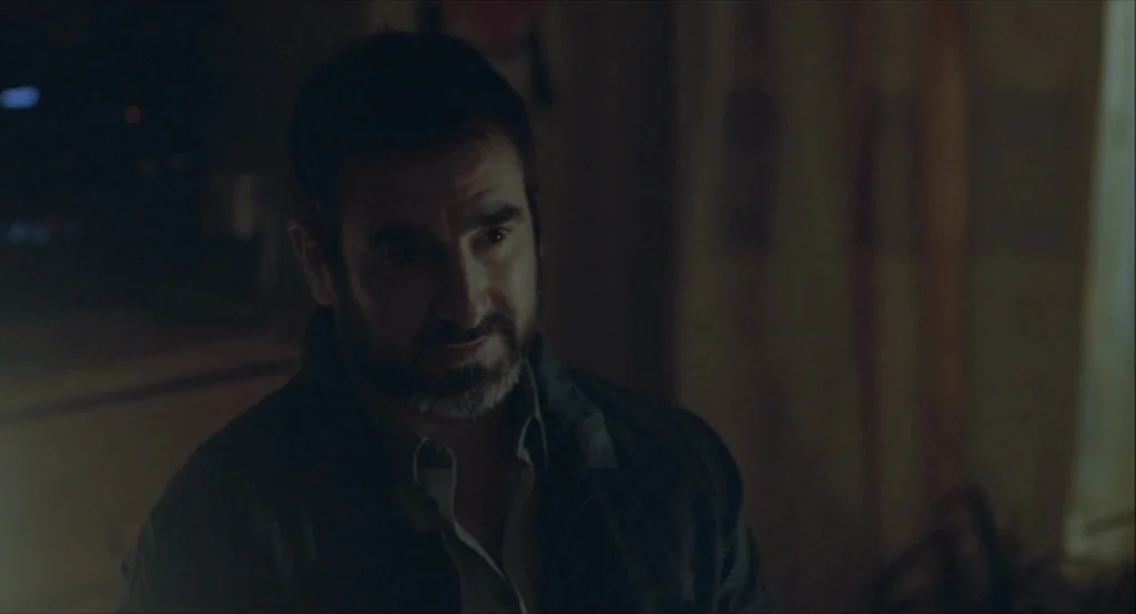 Looking for Eric (2009) movie still: closeup — A dimly lit room provides a dark, undifferentiated background behind the man. A man in his 40s sits…