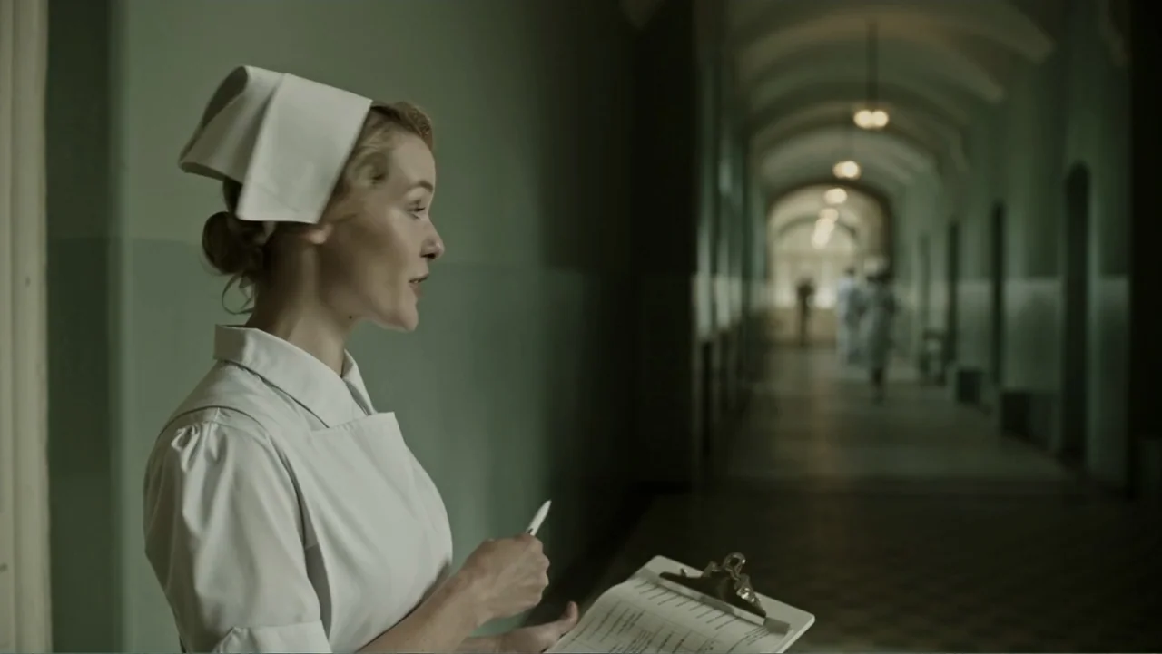 A Cure for Wellness (2017) movie still: medium — A long, arched hospital corridor features light green walls and an empty tiled floor. A woman…