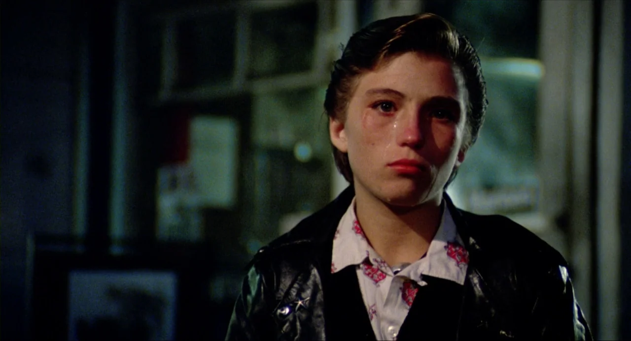 The Wanderers (1979) movie still: closeup — A dark night setting featuring an out-of-focus urban background with muted ambient lights. A teenage…