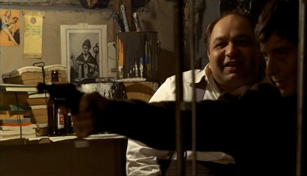 The Godfather (1972) movie still: medium — A cluttered room features stacks of paper, bottles, and a religious print on the wall. One man holds a…