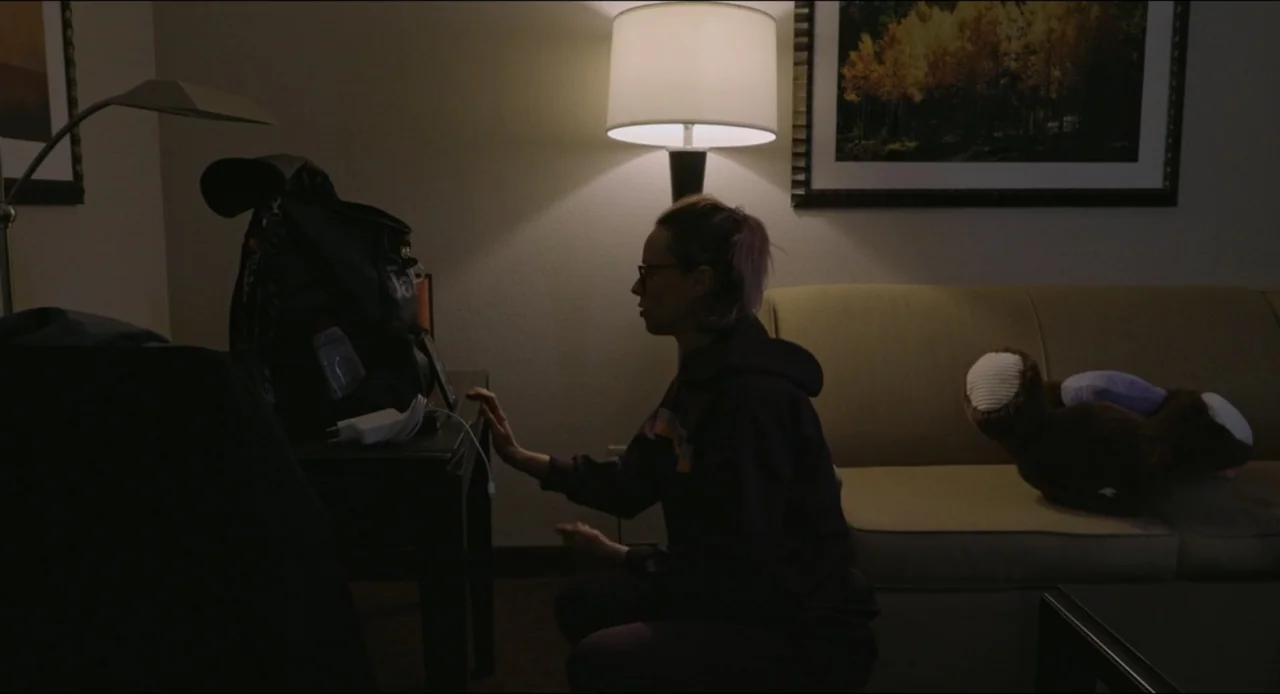 Federica Pellegrini - Underwater (2022) movie still: medium — A dark hotel room interior contains a sofa, a side table, and a floor lamp. A woman…