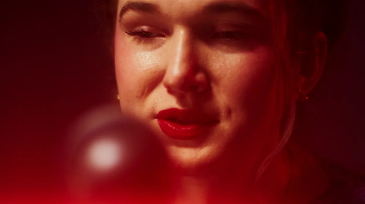 Carnage for Christmas (2024) movie still: closeup — A dark, minimally lit interior space is bathed in intense red light. A young woman with red…