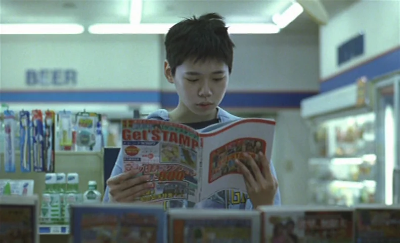 The Taste of Tea (2004) movie still: medium — A Japanese convenience store aisle is filled with shelves of products and fluorescent lighting. A…