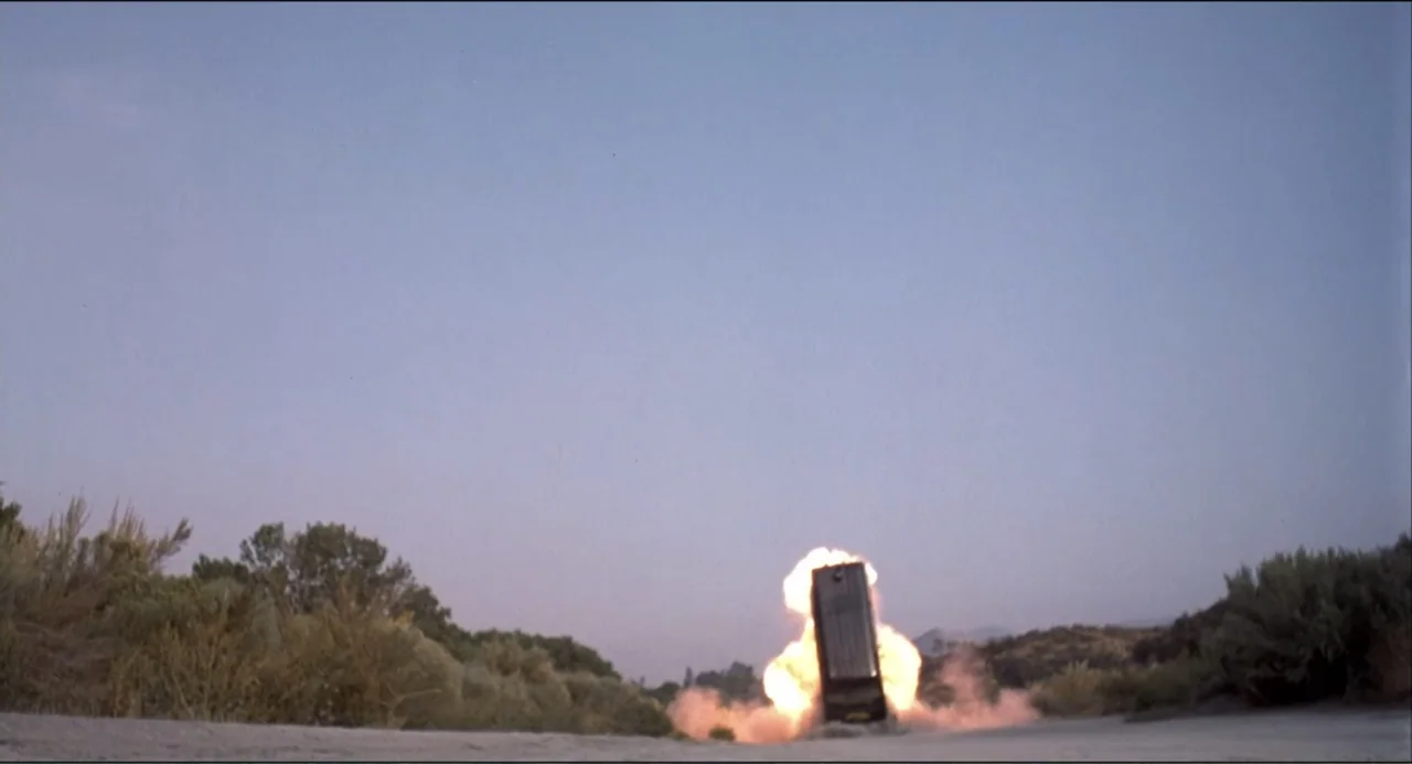 Air Rage (2001) movie still: wide — A desolate dirt road is flanked by dry desert scrub under a clear twilight sky. A single car is suspended…
