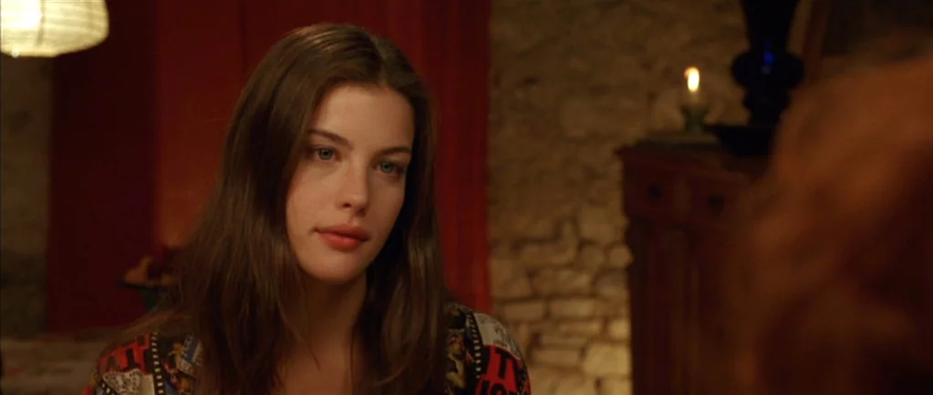 Stealing Beauty (1996) movie still: closeup — A dimly lit room with stone walls serves as the backdrop for the dialogue. A young woman with brown…