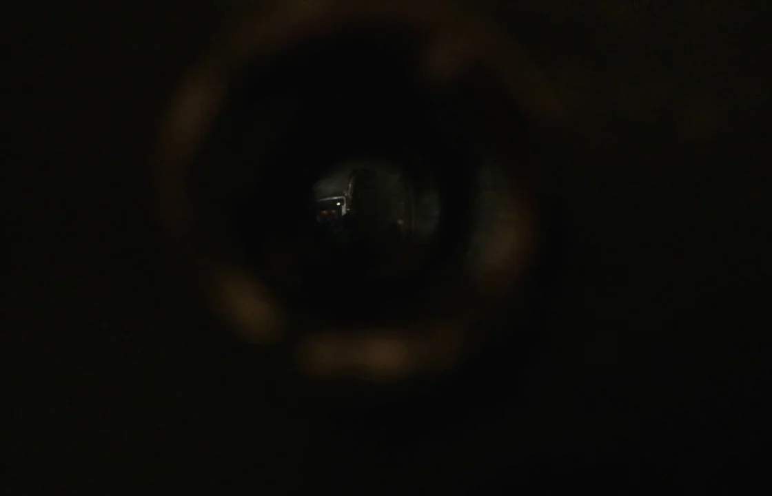 Unsane (2018) movie still: closeup — A circular view through a peephole reveals a dark and barely visible hallway interior. The edges of the frame…