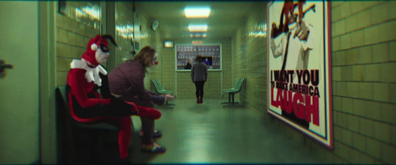 The People’s Joker (2022) movie still: wide — A long tiled hallway features a reception window at the far end and waiting benches. A large…