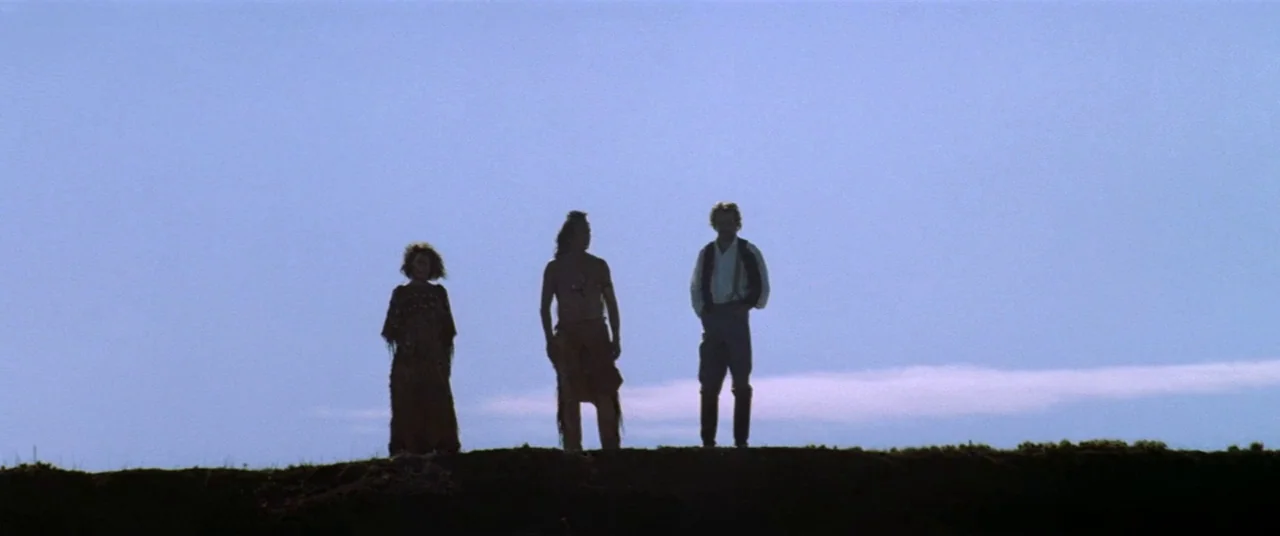 Dances With Wolves (1990) movie still: wide — Three individuals stand on a grassy ridge against a clear, expansive blue sky. The figures are…