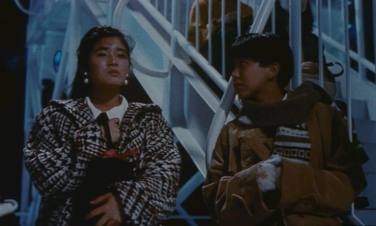 Chizuko’s Younger Sister (1991) movie still: medium — Two young people stand together on or near a white industrial-style exterior staircase. The…