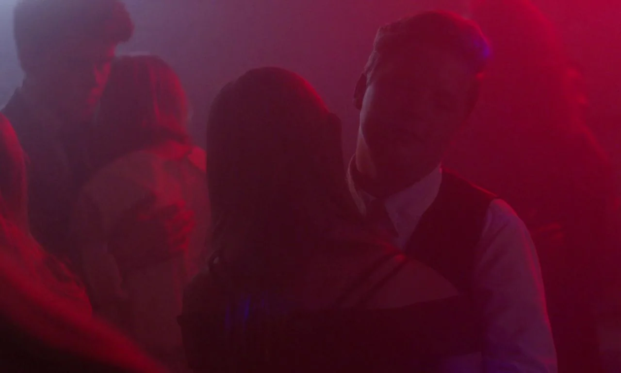 Ham on Rye (2019) movie still: medium — A dimly lit dance floor is obscured by thick haze and intense red light. A young man in a vest dances with a…