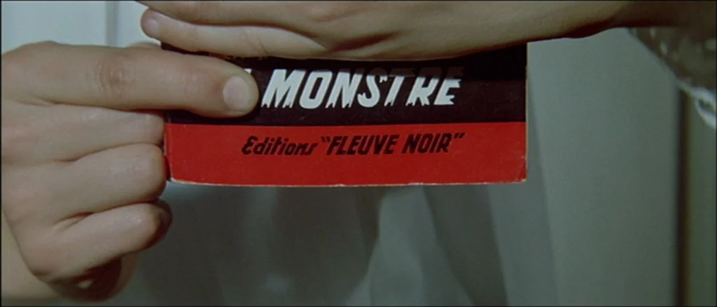 Une Femme Est Une Femme (A Woman Is a Woman) (1961) movie still: closeup — Close up of hands holding a paper book cover with red and black design.…