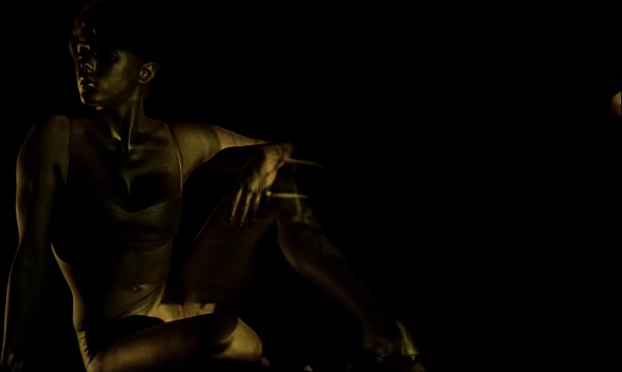Goldfinger (1964) movie still: medium — A woman sits in a void with extreme contrast between light and dark. She poses while bathed in a singular…