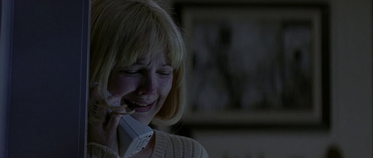 Scream (1996) movie still: closeup — A dimly lit room features a framed picture on the wall behind the subject. A young woman with blonde hair holds…