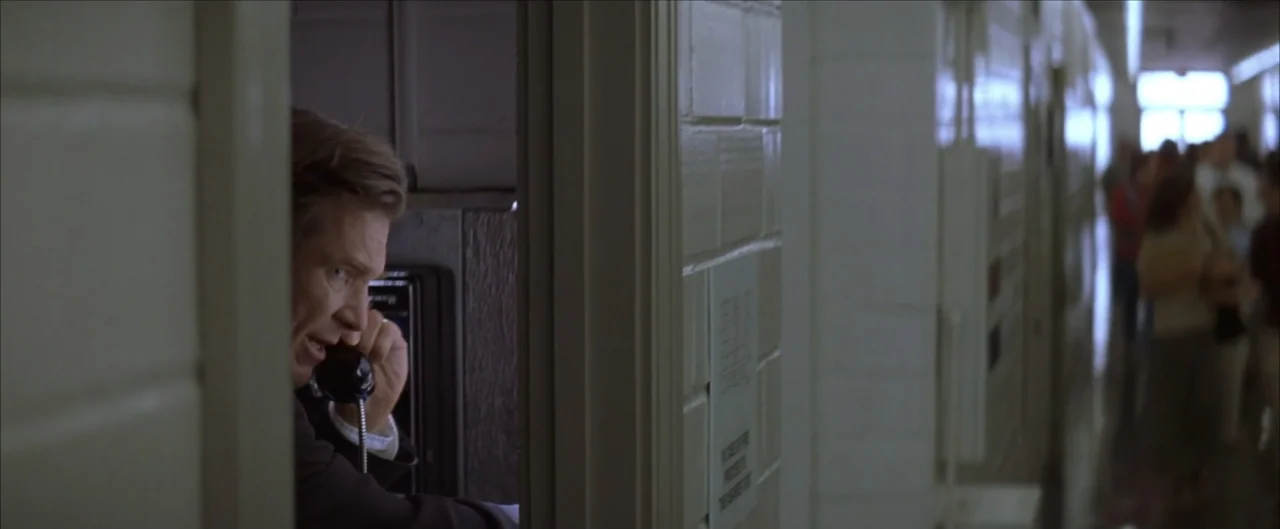 Arlington Road (1999) movie still: medium — A man in a suit stands inside a small booth using a public payphone. In the background, a brightly lit…