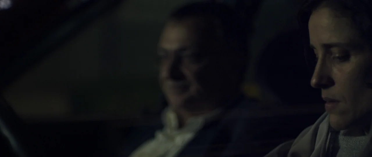 Alps (2011) movie still: medium — The interior of a vehicle at night with minimal ambient light. A woman sits in the foreground while an older man…